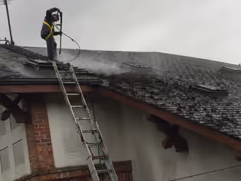 Couvreur harnaché nettoyant une toiture couverte de mousse sous la pluie
