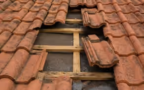 Trou dans une toiture en tuiles, plusieurs tuiles manquantes et liteaux à nu